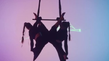 Modern koreografi ve akrobasi yaratıcı reklam konsepti. Kadın jimnastik düeti lazer neon stüdyo arka planında izole edildi. Kız dansçılar trapezde kayışlarla uçar, yakın çekim..