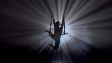 Modern koreografi ve akrobasi yaratıcı reklam konsepti. Kadın jimnastikçi siyah arka planda dumanla izole edilmiş. Kız hava dansçısı trapezde kayışlarla akrobasi gösteriyor, yakın çekim..