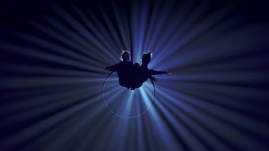 Modern koreografi ve akrobasi yaratıcı reklam konsepti. İki kadın jimnastikçi sahne ışıkları ve dumanla siyah arka planda izole edilmiş. Hava dansçıları yüzükteki elementi kayışlarla gösteriyorlar.