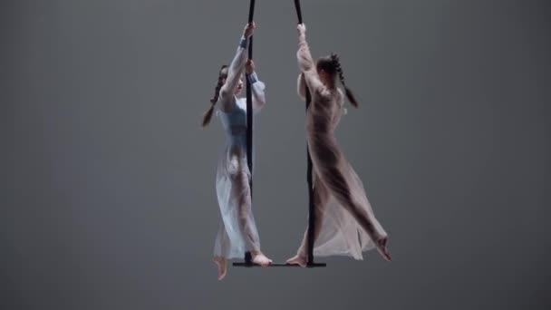 現代の振付とアクロバットクリエイティブ広告コンセプト 女性の体操デュオは灰色のスタジオの背景で孤立しました ストラップ付きアクロバットトラップで踊る少女空中ダンサー ショットを閉じる — ストック動画
