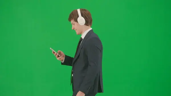 现代商人创意广告的概念 彩色键绿色荧幕上的男模肖像 穿着时髦西装的英俊商人在耳机里用智能手机听音乐 — 图库照片