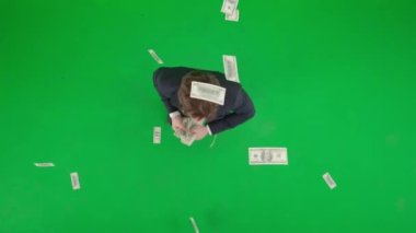 Modern iş adamı yaratıcı reklam konsepti. Krom anahtar yeşil ekranda erkek modelin üst görüntüsü. Takım elbiseli bir işadamı elinde banknotlarla dans ederken havaya fırlatıyor. Yavaş çekim.