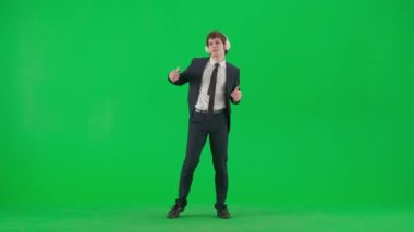 Modern iş adamı yaratıcı reklam konsepti. Krom anahtar yeşil ekranda erkek modelin portresi. Takım elbiseli yakışıklı genç işadamı kulaklıkla müzik dinliyor, akıllı telefonda dans ediyor..