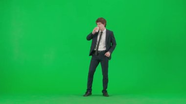 Modern iş adamı yaratıcı reklam konsepti. Krom anahtar yeşil ekranda erkek modelin portresi. Güzel takım elbiseli yakışıklı genç işadamı elinde kahve içip dans ediyor.