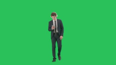Modern iş adamı yaratıcı reklam konsepti. Krom anahtar yeşil ekranda erkek modelin portresi. Modayı takip eden takım elbiseli yakışıklı iş adamı kulaklıkla akıllı telefondan müzik dinliyor..