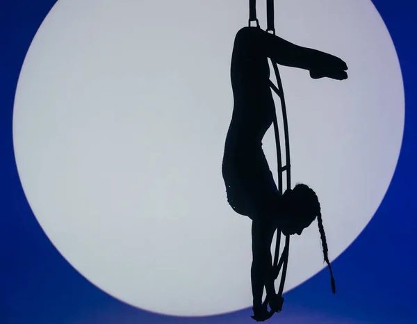 女性空中体操运动员的轮廓在蓝光下挂在月亮上 中间有聚光灯 杂技演员展示了在月球上表演的元素 空中体操的概念 — 图库照片