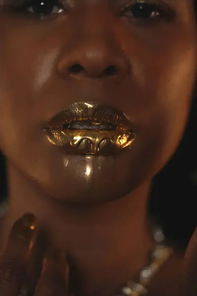Portrait of a young African American woman with a gold necklace around her neck. Liquid gold is applied to the models lips and flows down in thin streams. Beauty concept. Close up