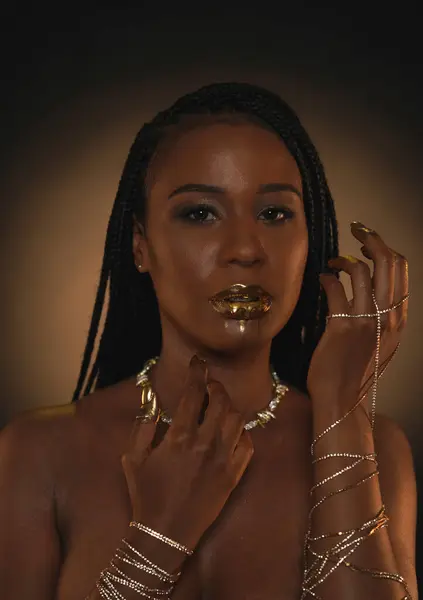 Portrait of a young African American woman with gold chains on her hands and a necklace on her neck. Liquid gold is applied to the models lips and flows down in thin streams. Beauty concept. Close up