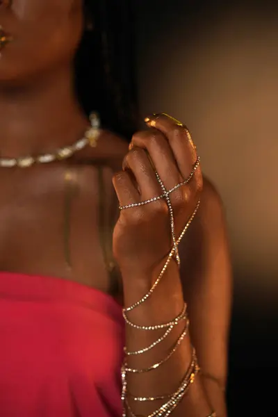 An African American womans hand is entwined with a gold chain. Streaks of liquid gold are visible on the shoulder. Close up. Beauty concept