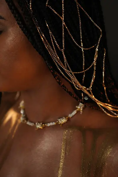 Portrait of an African-American woman with a gold necklace and gold chains in her hair. The models collarbones are covered with liquid gold. Close up. The concept of beauty