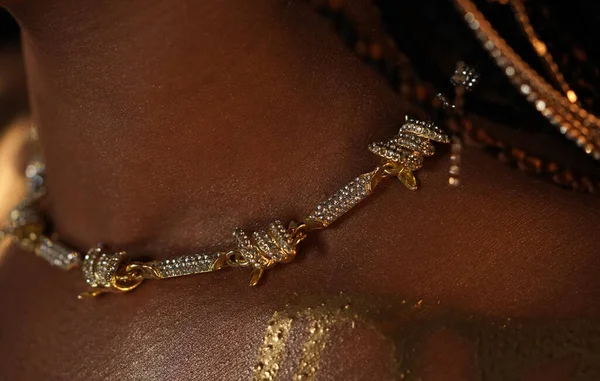 Close up of the neck and shoulder of an African American woman wearing a gold necklace and streaks of liquid gold. The models skin shines and shimmers in the studio light. Beauty concept