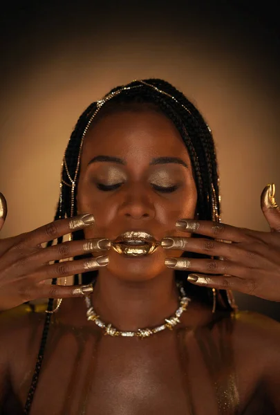 Portrait of an African-American woman with a gold necklace and gold chains in her hair. The models lips, fingers and nails are covered with liquid gold. Close up. The concept of beauty