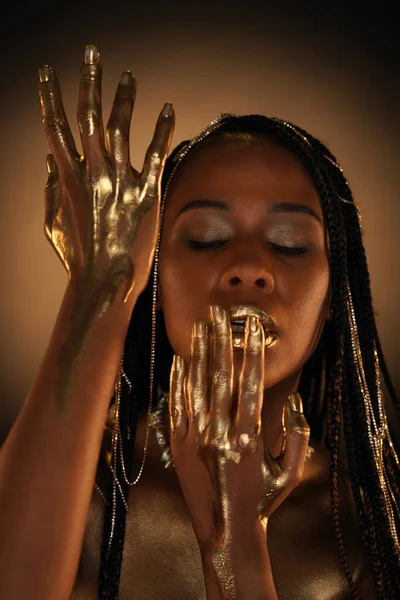 Portrait of an African-American woman with gold chains in her hair. Liquid gold is flowing down the models arms. Close-up. The concept of beauty