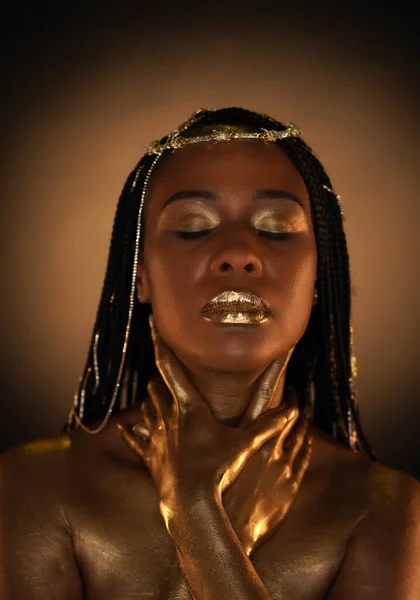 Portrait of an African-American woman with gold jewelry in her hair. The models arms, neck and shoulders are covered with liquid gold. Close-up. The concept of beauty