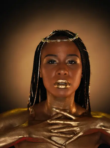 Portrait of an African-American woman with gold jewelry in her hair. The models arms, neck and shoulders are covered with liquid gold. Close-up. The concept of beauty
