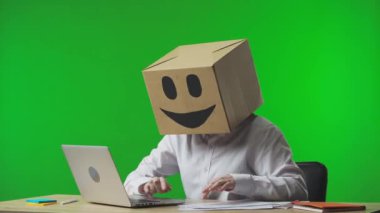 Stüdyonun yeşil arka planında gülümseyen emojisi olan mukavva kutudaki kadın. Çalışan, belgelerdeki ve laptoptaki verileri kontrol ediyor ve başarısına seviniyor. İş hayatı.