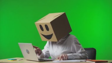 Stüdyonun yeşil arka planında gülümseyen emojisi olan mukavva kutudaki kadın. Çalışan, belge ve dizüstü bilgisayardaki verileri kontrol eder, başarıya sevinir ve onaylar. İş hayatı.
