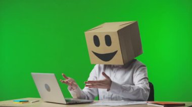 Stüdyonun yeşil arka planında gülümseyen emojisi olan mukavva kutudaki kadın. İşçi dizüstü bilgisayarına bakar ve başarı, iyi haber ya da kazanma konusunda mutludur. İş hayatı.