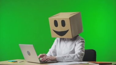 Stüdyonun yeşil arka planında gülümseyen emojisi olan mukavva kutudaki kadın. Kadın işçi bir klavyeye yazı yazıyor ve baş parmak işareti yapıyor. İş hayatı.