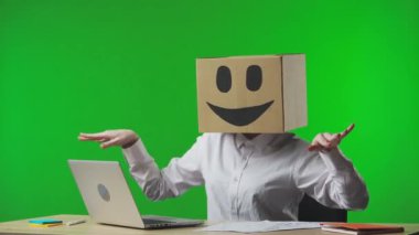 Stüdyonun yeşil arka planında gülümseyen emojisi olan mukavva kutudaki kadın. İşçi olumlu bir hareket gösterir ve başarı, iyi haber ya da kazanma konusunda mutludur. İş hayatı.