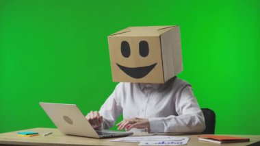 Stüdyonun yeşil arka planında gülümseyen emojisi olan mukavva kutudaki kadın. Çalışan, belge ve dizüstü bilgisayardaki verileri kontrol eder, başarıya sevinir ve onaylar. İş hayatı.