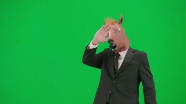 Yeşil stüdyo geçmişinde at kafası maskesi olan takım elbiseli bir adam. İş adamı yürüyor ve el sallıyor. Ofis işi kavramı Yarım tur