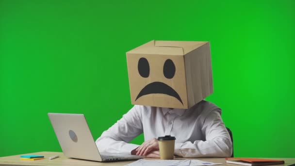 头戴纸板箱的女人背景是绿色的工作室有悲伤情绪的员工正在喝咖啡 把盒子翻过来变成微笑的情绪 兴高采烈地打字 — 图库视频影像