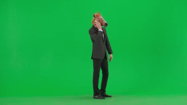 一个穿着西装 戴着马头面具 背景为绿色工作室的男人 一位商人正在用智能手机交谈 他很生气 对着电话大喊大叫 艰苦工作概念 — 图库视频影像