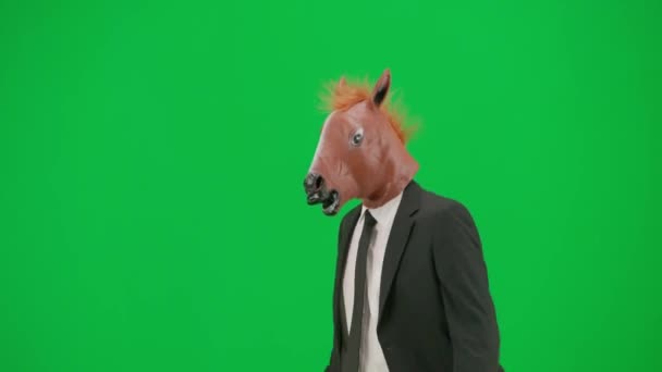 グリーンスタジオの背景に馬のヘッドマスクとビジネスススーツの男 ビジネスマンウォーキング バウンス ダンス ハードオフィスのコンセプト ハーフターン — ストック動画