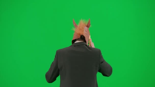 身穿西装 头戴马头面具 背景是绿色工作室 商人一边走路一边用智能手机说话 艰苦工作的概念回顾 — 图库视频影像