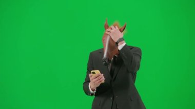 Yeşil stüdyo geçmişinde at kafalı maskeli bir iş adamı. Bir iş adamı akıllı telefonundan bir şeye bakıyor ve kaybettiği için üzgün. Sıkı çalışma konsepti