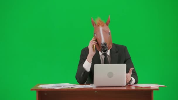 身穿西装 头戴马头面具 背景为工作室绿色 商人坐在办公桌前 用智能手机交谈 非常生气 重型办公室工作概念 — 图库视频影像