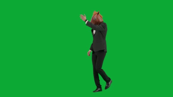 グリーンスタジオの背景に馬のヘッドマスクとビジネスススーツの男 ビジネスマンが歩き 挨拶をする ハードオフィスのコンセプト ハーフターン — ストック動画