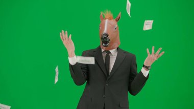 Yeşil stüdyo geçmişinde at kafalı maskeli bir iş adamı. İşadamı mutlu bir şekilde para saçıyor. Sıkı çalışma konsepti