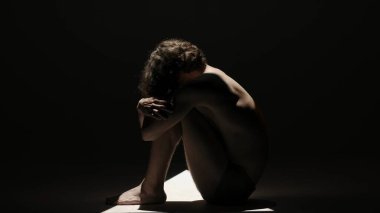 Vücut güzelliği ve sağlık hizmetleri yaratıcı reklam konsepti stüdyoda siyah arka planda erkek modelin portresi. Yerde poz veren çekici bir adam silueti. Yan görünüm