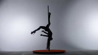 Direk dansı. Beyaz bir arka planda spot ışıkları altında karanlık bir stüdyoda akrobatik elementler sergileyen bir kızın silüeti.