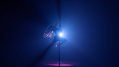 Esnek ve plastik bir kadının karanlık silueti direğin üzerinde dans ediyor. Karanlık bir stüdyoda, parlak bir ışığa karşı direkte dans eden bir kadın.