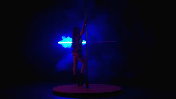 撑杆跳年轻女子在黑暗的演播室里 在蓝色霓虹灯的映衬下 冒着浓烟跳舞 女人跳脱衣舞穿着高跟鞋的性感女人 — 图库照片