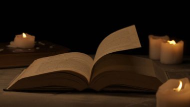 Tarihi ve klasik nesneler yaratıcı reklam konsepti. Karanlık arka plan ve sıcak ışık üzerine eski bir ciltli kitabın stüdyo çekimi. Rüzgâr esiyor sayfalarca eski kitap, etrafında mumlar..