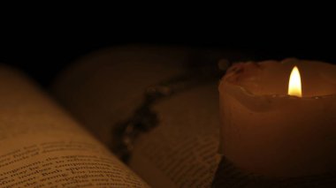 Tarihi ve klasik nesneler yaratıcı reklam konsepti. Karanlık arka plan ve sıcak ışık üzerine eski bir ciltli kitabın stüdyo çekimi. Masanın üzerinde mum ve haç döşenmiş eski moda bir kitap..