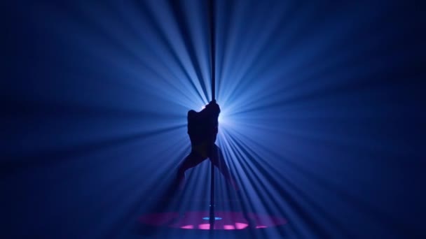 一个倒立在塔上的女人的黑暗轮廓 在昏暗的演播室里 女人在一根柱子上迎着明亮的灯光跳舞 — 图库视频影像
