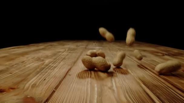 坚果和香料创意广告的概念 在工作室的木制表面上近距离拍摄食物配料 许多新鲜烘烤的未剥皮花生掉在桌子上 滚在地上 — 图库视频影像
