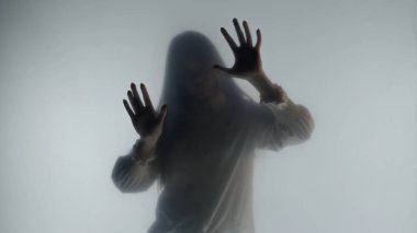 Şeffaf bir buzlu perde ya da camın arkasında melankolik bir kadın silueti. Bir kadın avuçlarıyla perdenin yüzeyine dokunuyor.