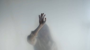 Melankolik kadın silueti şeffaf bir buzlu perde ya da camın arkasında. Bir kadın elini perdenin üstünde gezdiriyor.