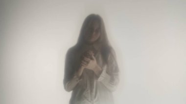 Donmuş perde ya da camın arkasında beyaz elbiseli bir kızın silueti. Üzgün bir kadın başı öne eğik durur. Mistik konsept