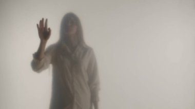 Melankolik kadın silueti şeffaf bir buzlu perde ya da camın arkasında. Bir kadın elini perdenin üstünde gezdiriyor.