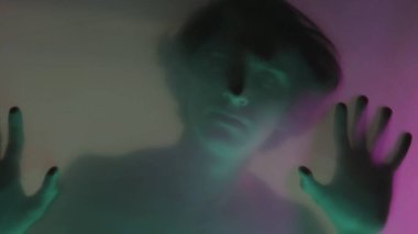 Mat bir perdenin arkasında çıplak gövdesi olan, yeşil neon ışıklı bir adamın bulanık silueti. Adam şeffaf bariyere dokunuyor, kurtulmaya çalışıyor. Hayaletler konsepti...