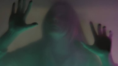Paspas perdesinin arkasında, pembe ve yeşil neon ışıklı bir kadının bulanık silueti. Yaklaş. Bir kadın tırnaklarını bariyere sürtüyor, yırtmaya çalışıyor. Hayaletler ve ruhlar kavramı