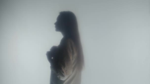 白いブラウスの金髪の女性のボタンのボタンのシルエットの側面の景色 明確な曇らされたガラスまたはカーテンの後ろの蒸気または霧の女性のプロフィールの肖像画 — ストック動画