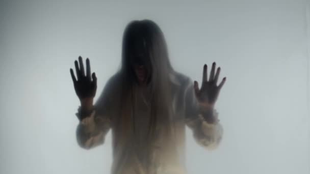 曇ったガラスかカーテンの後ろの霧のパニックな女性のシルエット 女性は透明で目に見えない障壁に対して頭を叩きます 死後の世界 霊の概念 — ストック動画